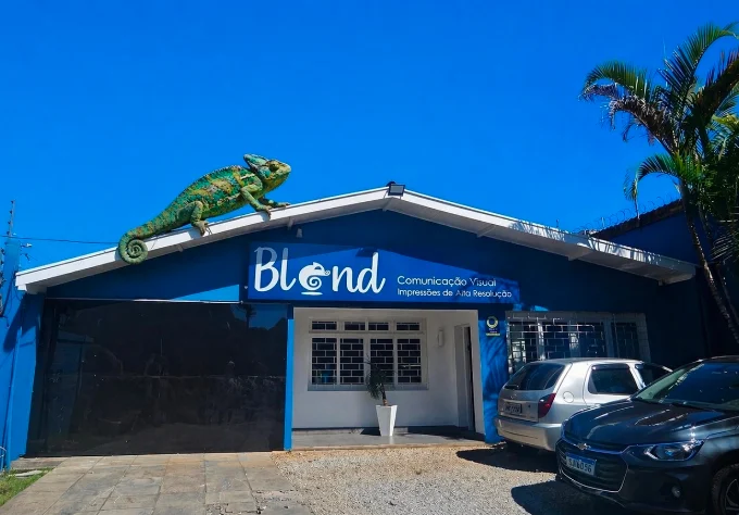 Fachada azul da Blend Comunicação Visual com letreiro e uma grande escultura de camaleão verde sobre o telhado